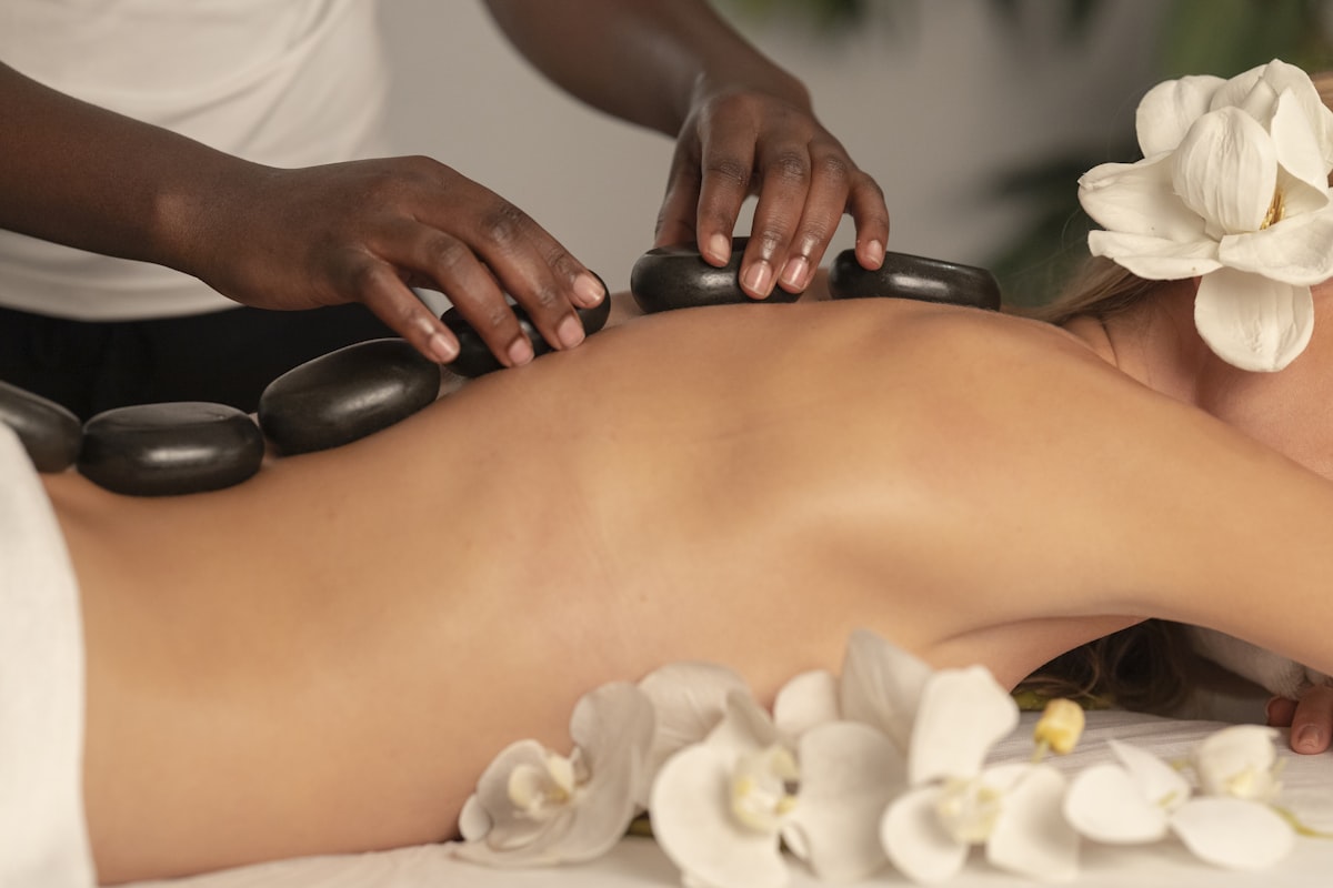 Hot stone massage treatment with white flowers, evoking Chakras' relaxation therapies